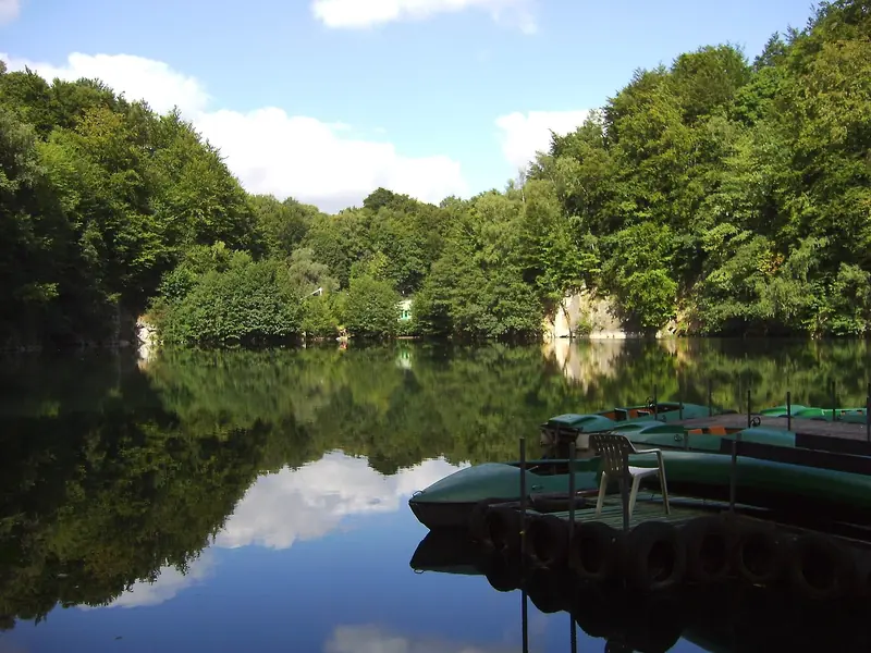 Der Blaue See in Ratingen mit bewaldeten Felswänden und Ruderbooten am Ufer