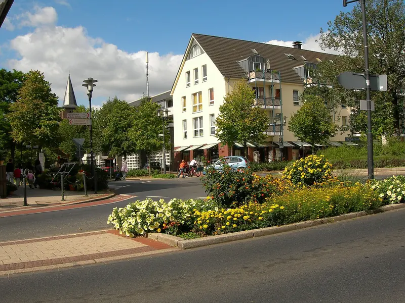 Ortsmitte von Ratingen-Hösel mit Blumenbeet, Wohnhaus und Kirchturm im Hintergrund
